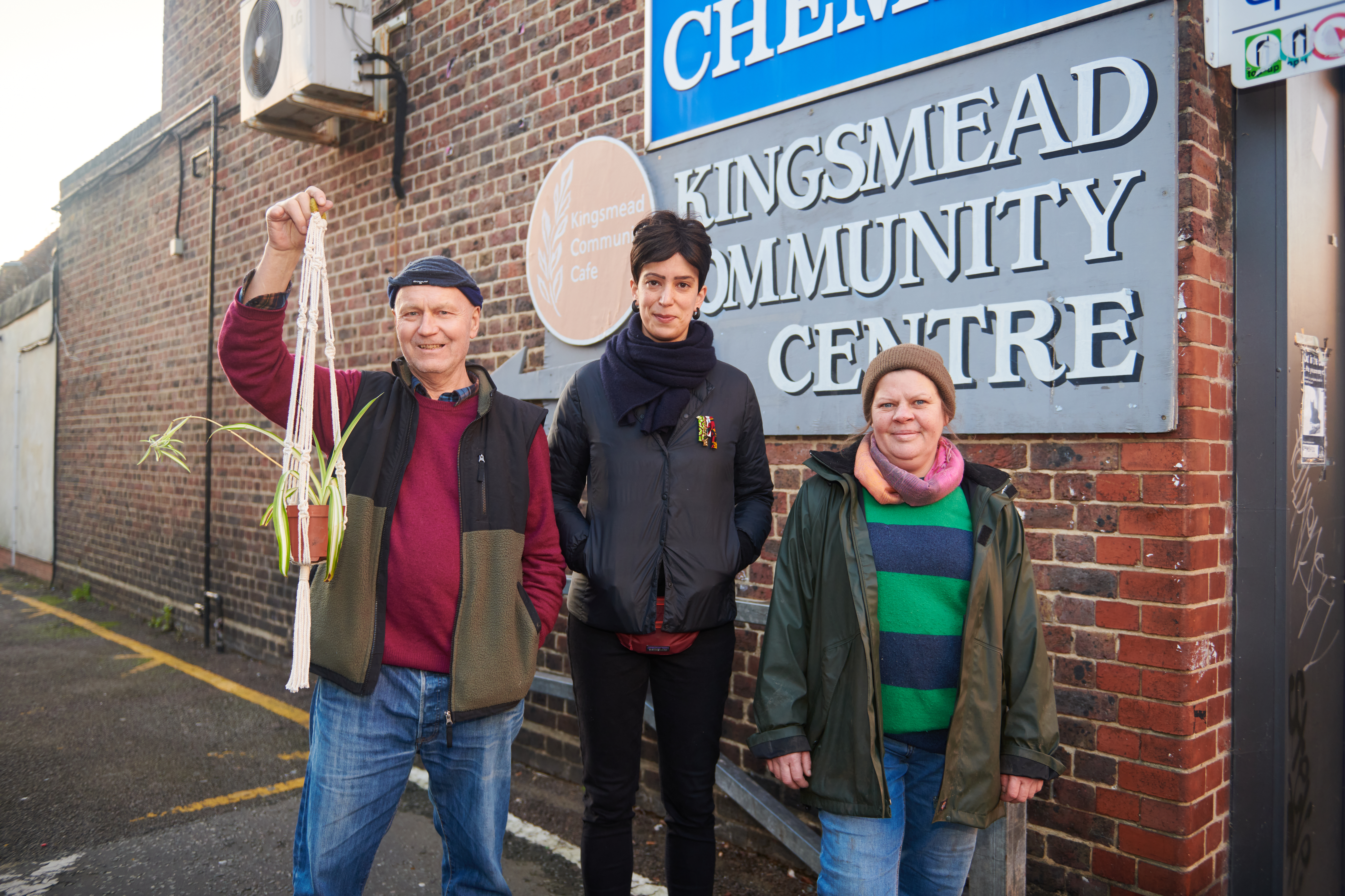 Kingsmead Community Centre gardening group Three people are shown in front of a sign reading Kingsmead Community Centre