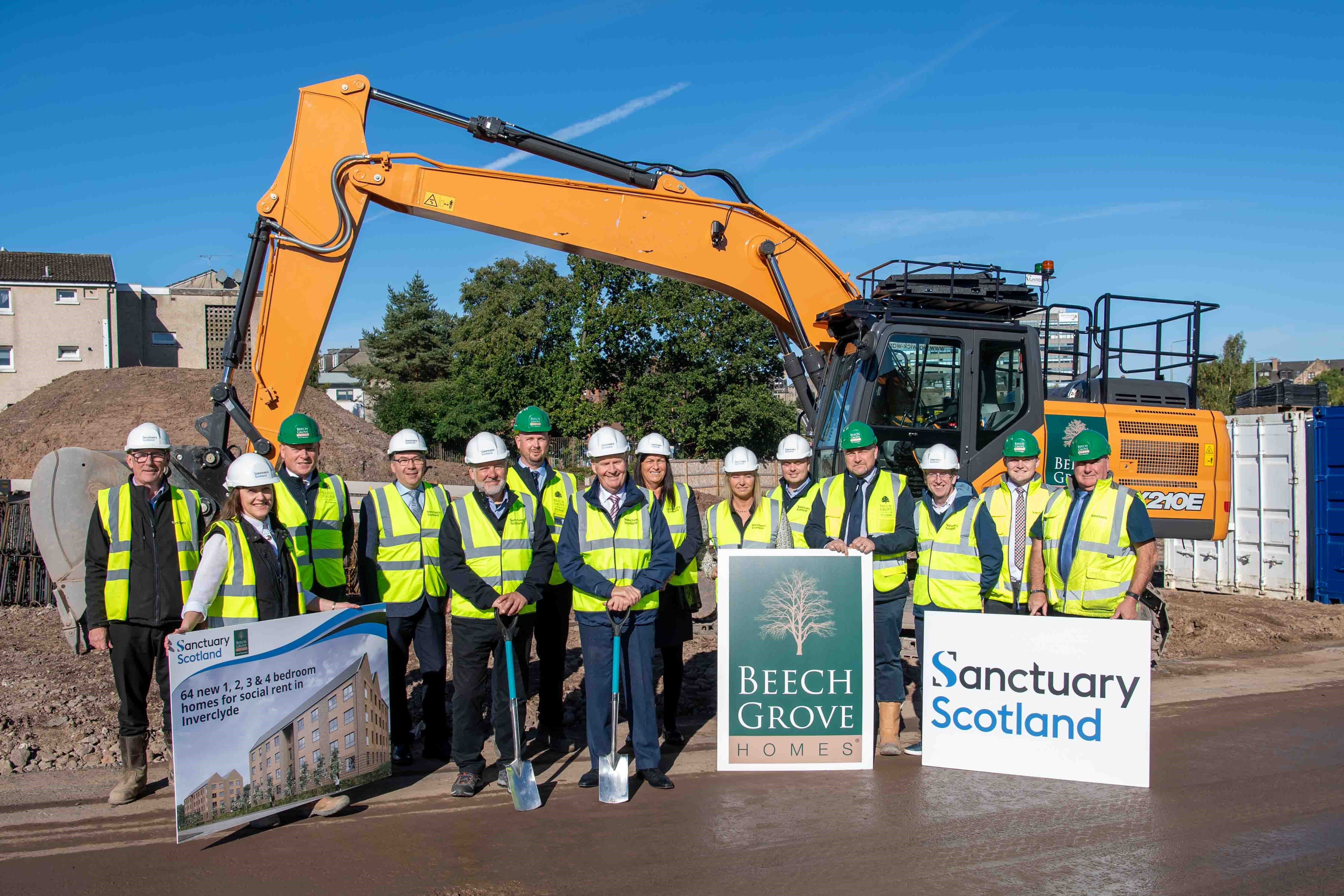A group of 14 people wearing high vis and hard hats stood in front of a housing development site on a sunny day