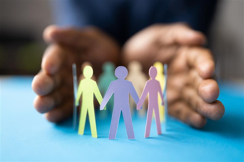A circle of different coloured silhouettes of people cut out of paper with a pari or hands surrounding them