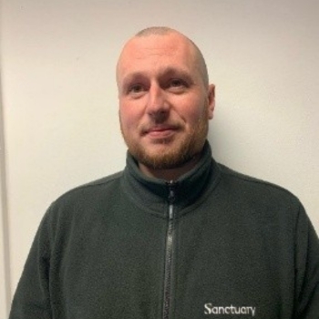 Headshot of a man smiling at the camera wearing his Sanctuary work uniform