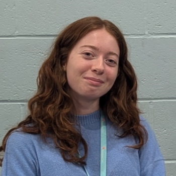Headshot photo of woman with long hair, wearing a Sanctuary lanyard and smiling at the camera