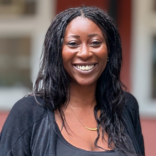 A smiling woman with long dark hair stands in front of a block of flats