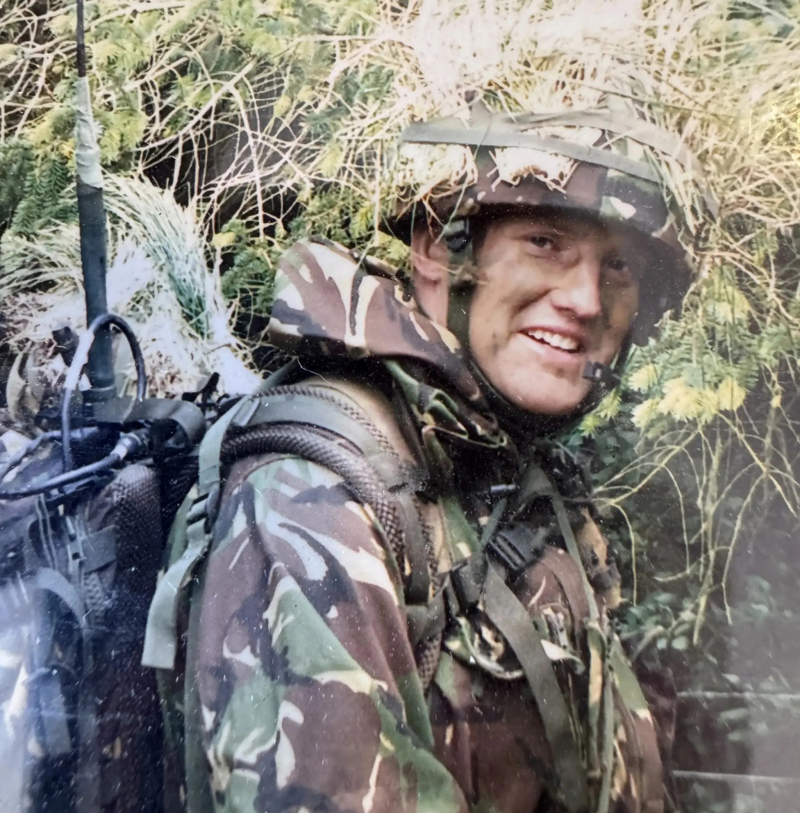An archive photo of Tristram Channer during his time with the Armed Forces. He is wearing camouflage gear and a helmet.