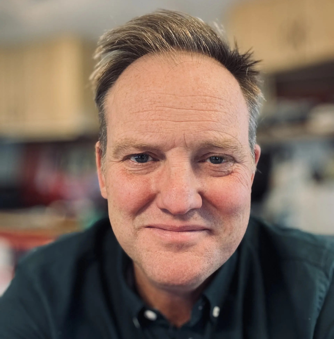 A head and shoulders photo of Tristram Channer today, working for Sanctuary. He is looking towards the camera and smiling. He has short, light brown hair and is wearing a dark button-up shirt.