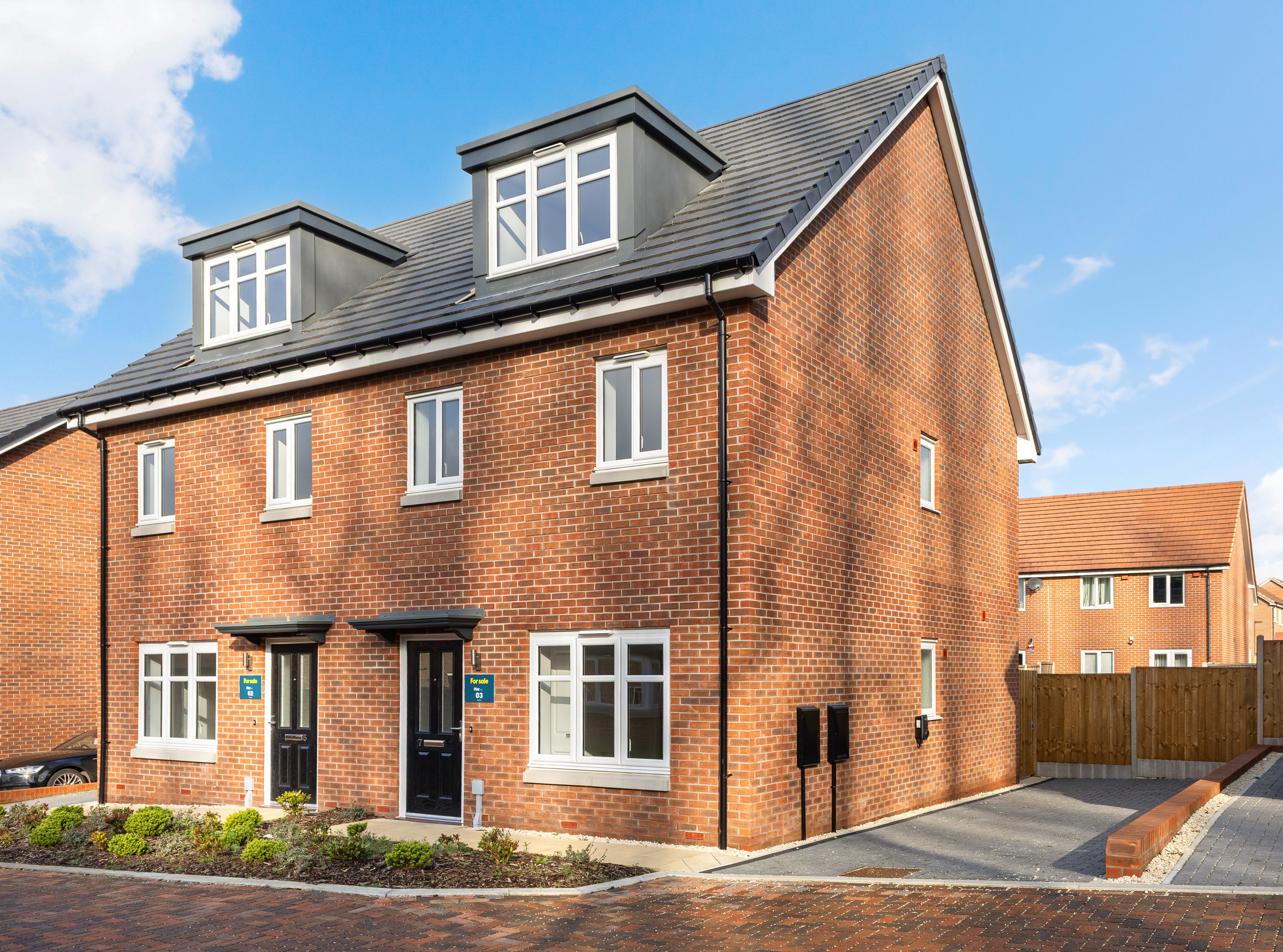 Front view of a red brick semi-detached house with white windows and a black front door.