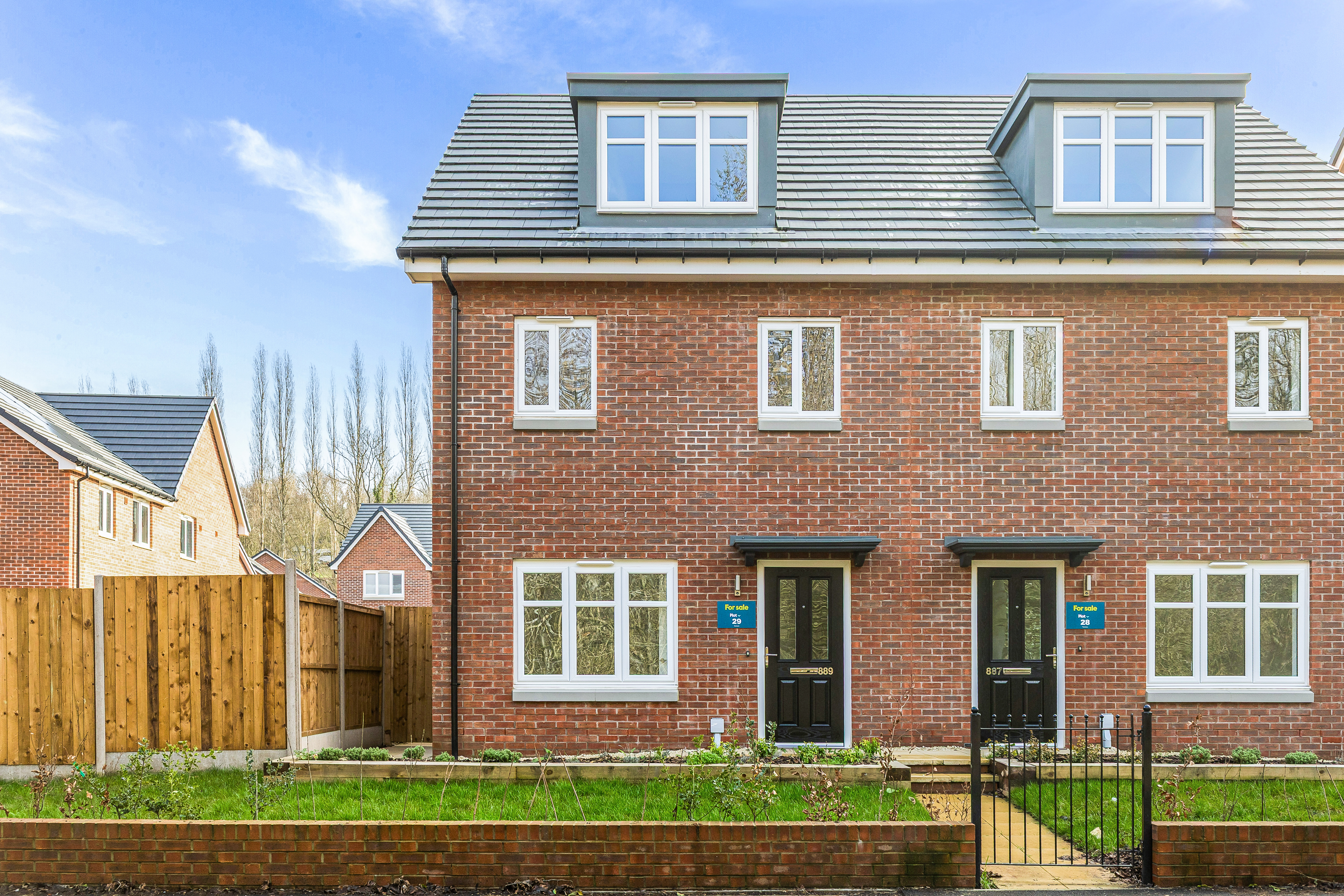 Front view of a red brick semi-detached house with white windows and a black front door.