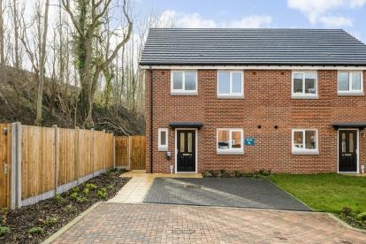 Front view of a red brick semi-detached house with white windows, black front doors and block paved driveway.
