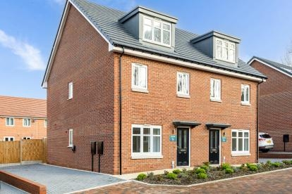 Front view of a red brick semi-detached house with white windows, a black front door and driveway on the left side of the house.