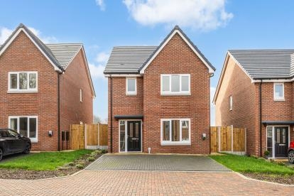 Front view of a red brick detached house with white windows, a black front door and block paved driveway.