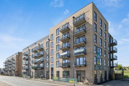 Modern brick apartment building with multiple floors, featuring glass-fronted balconies and large windows, set along a street under a clear blue sky, with signage for “Gateway House” and shared ownership homes visible on the exterior.