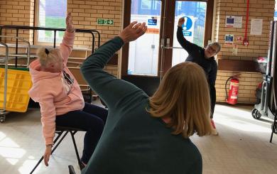 An instructor gets people moving and stretching in a gentle chair yoga session.