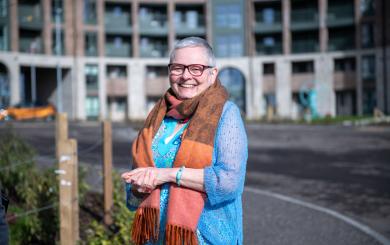 A woman smiling in front of a block of flats