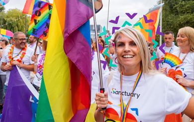 Sanctuary staff and residents wearing white shirts with rainbow hearts on carrying rainbow flags taking part in a march for a PRIDE event