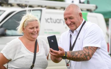 Two people chatting near a white van—one shows something on their phone. The van says “A better life, no conditions.”
