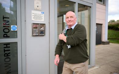Person wearing a green sweater and beige trousers exiting a building labeled 'Rockworth Point'