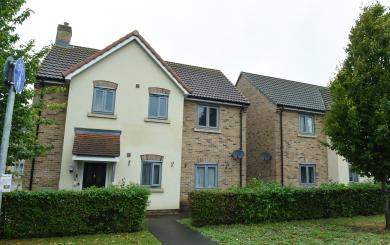 Two modern semi‑detached houses with cream and brick walls, grey windows, hedges and a footpath in front.
