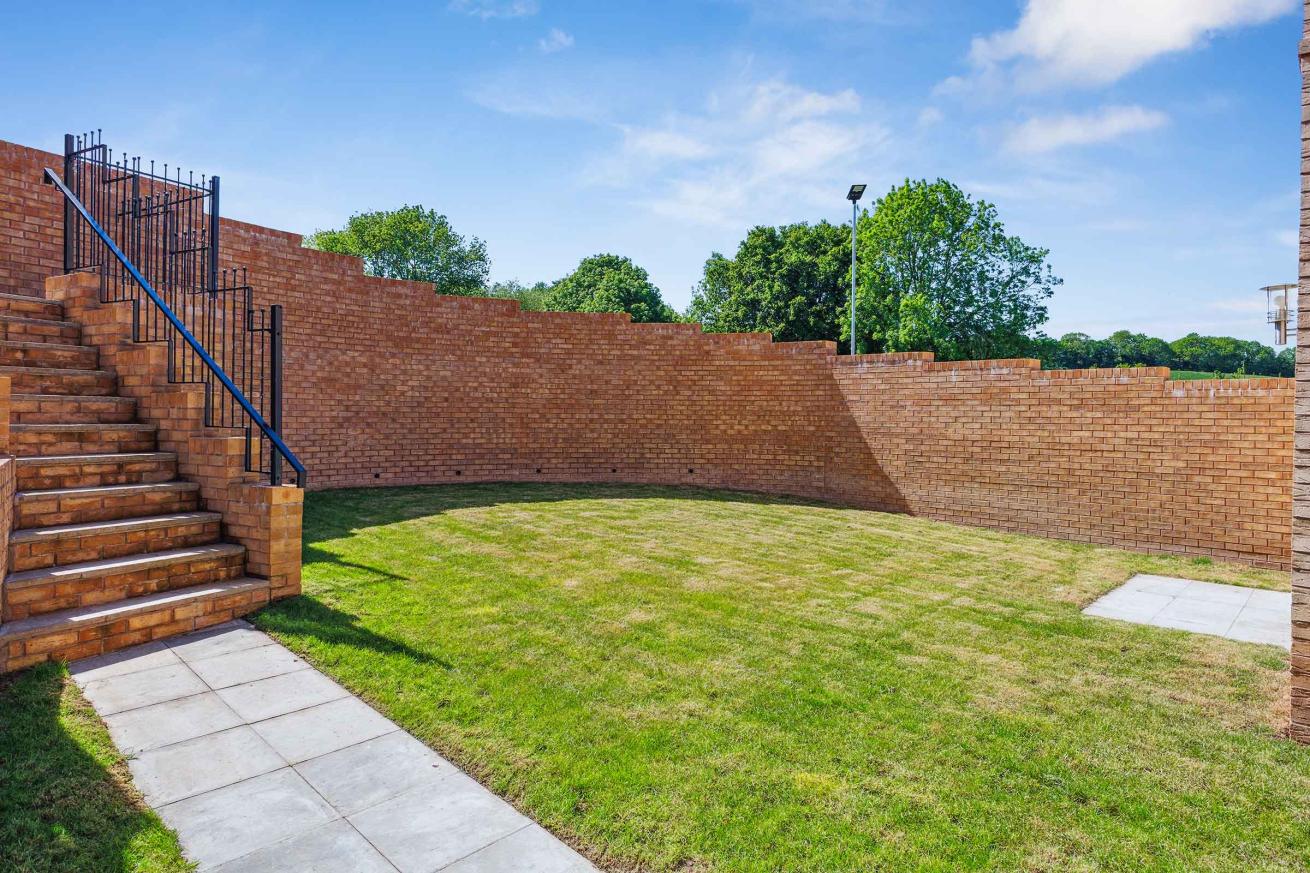  Enclosed garden with brick walls, grass lawn, and steps leading up to a gate.