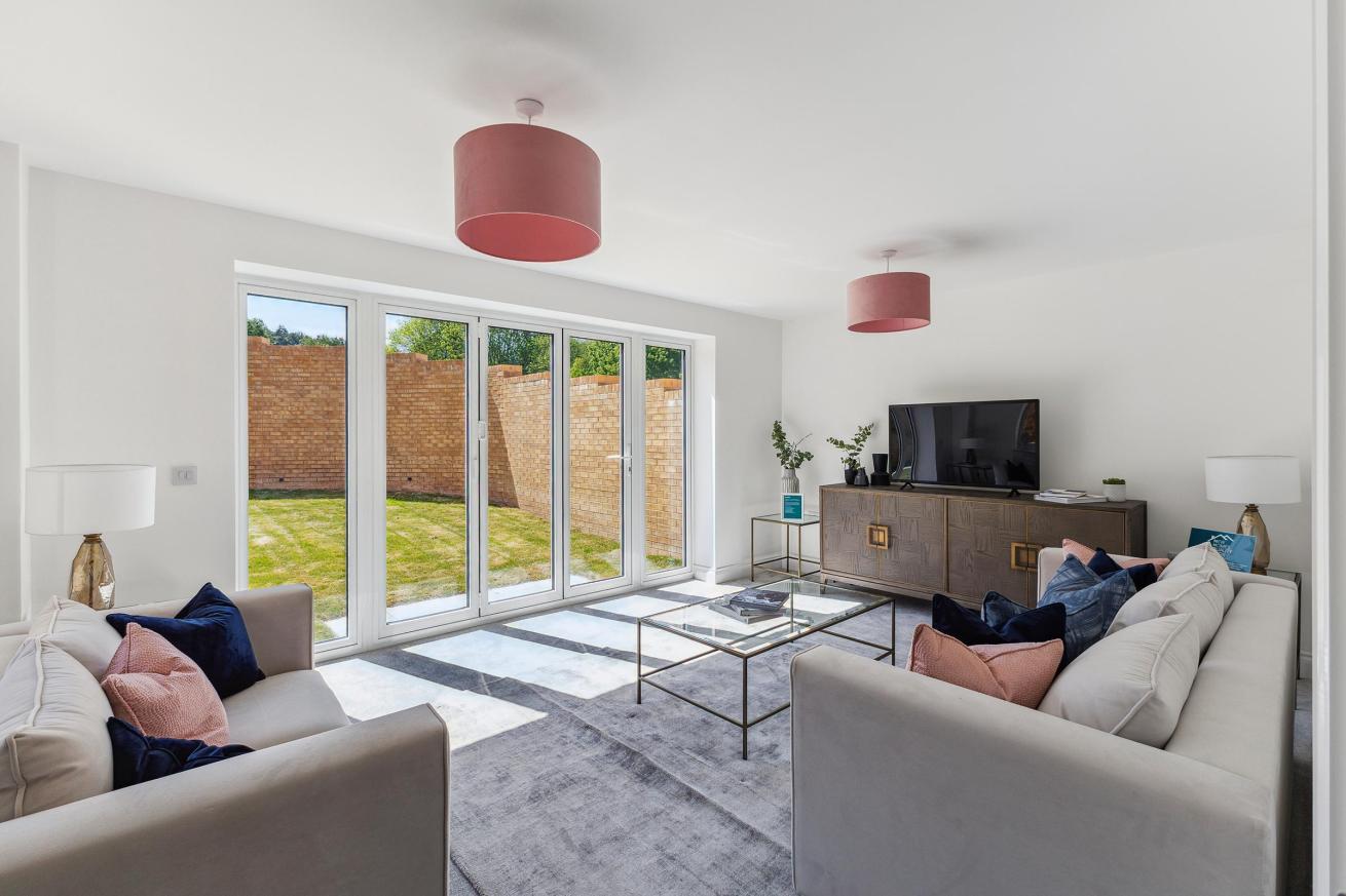 Living room with two sofas, coffee table, TV unit, and glass doors to garden.
