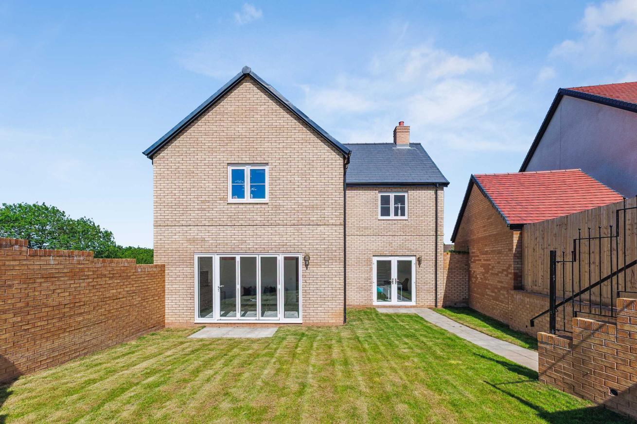  Rear garden view of a modern brick house with large glass doors and a lawn.