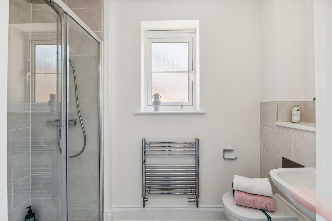 Compact shower room with glass shower enclosure, window, and towel rail.