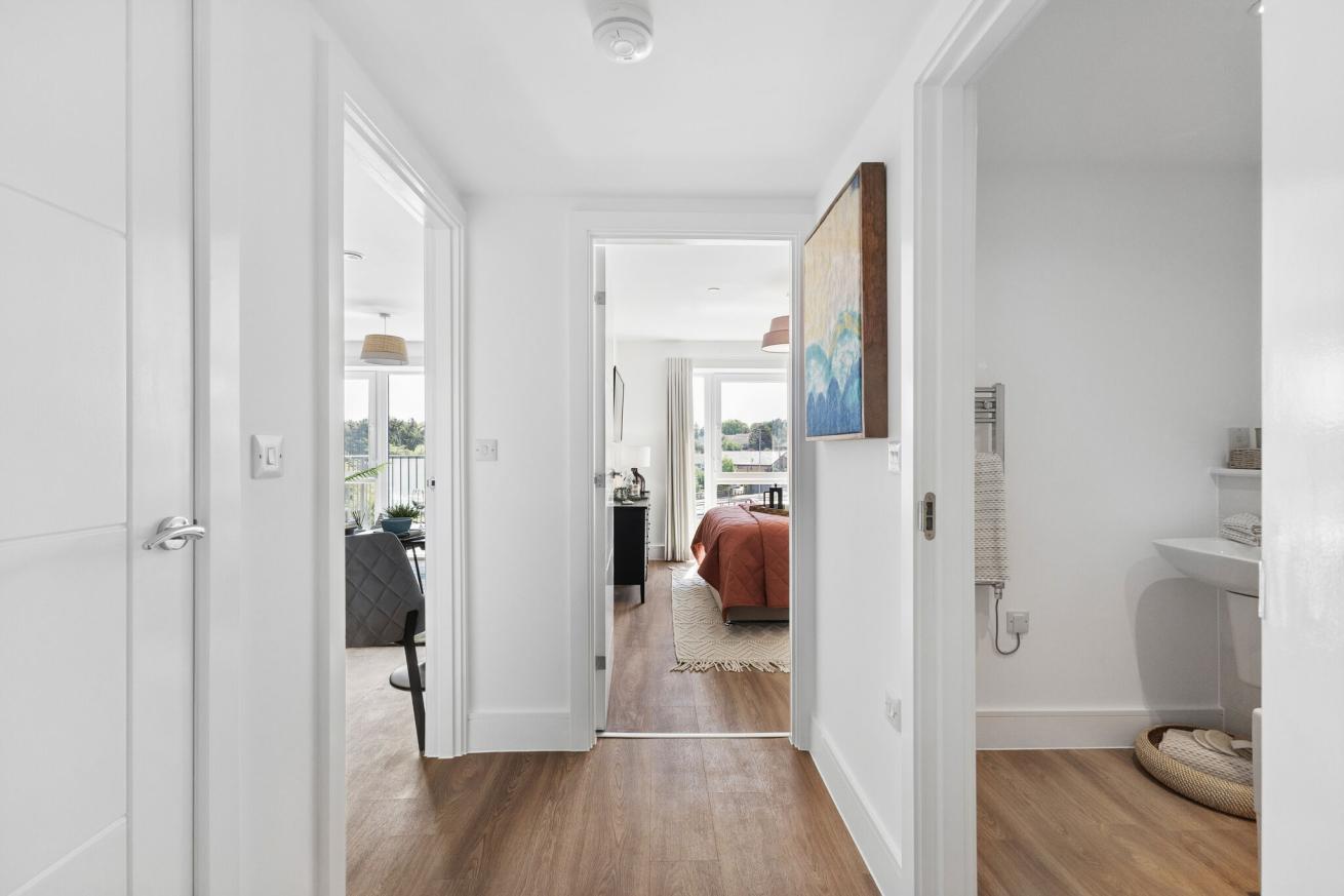 New build hallway in an apartment with doors leading to a bathroom, bedroom and living room. There is modern wooden flooring throughout