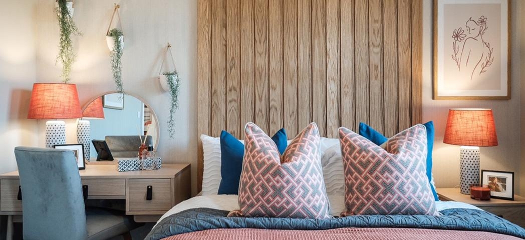 A double bedroom decorated in pastel colours with wooden panelling behind the bed and a desk in the corner