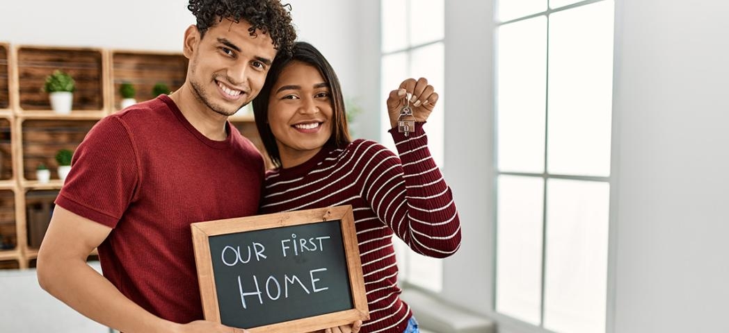 Two people holding a chalkboard saying our first home and holding keys
