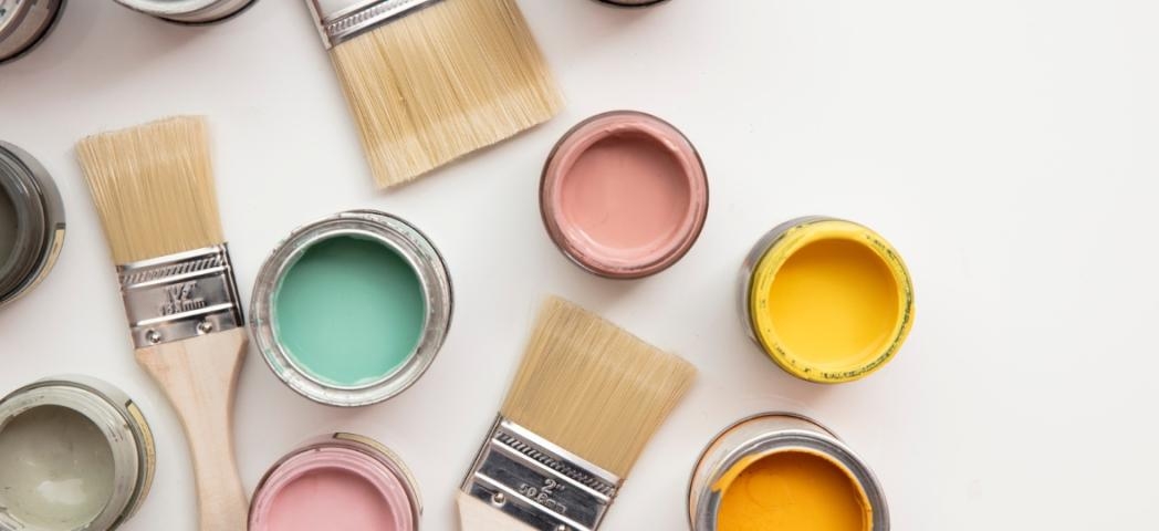 A collection of open paint pots of bright colours with several paintbrushes