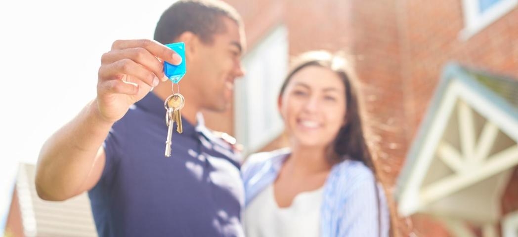 A couple stood outside a house in an embrace holding keys