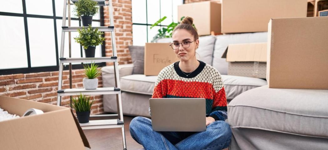 A person sat on the floor of their home after moving in, surrounded by moving boxes.