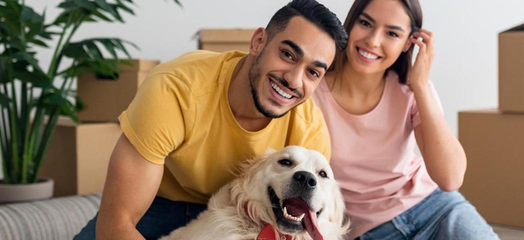 Two people sat with a dog in front of moving boxes 