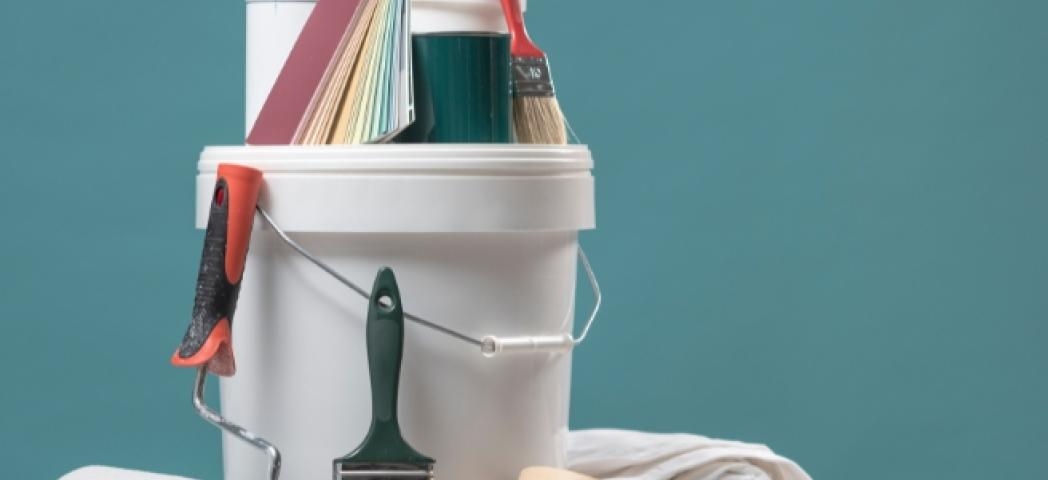 A tub of paint and paintbrushes against a newly painted blue wall