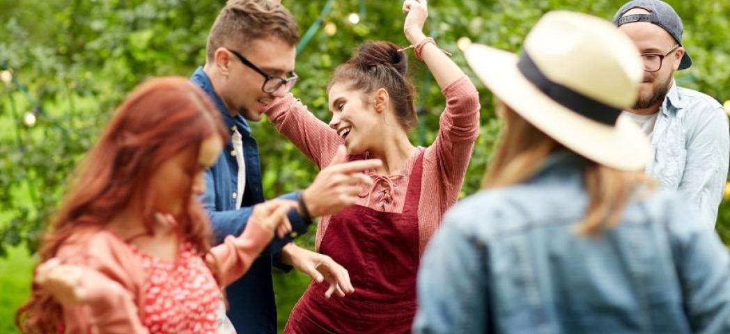 A group of men and women dancing in a garden decorated with multicoloured bunting.