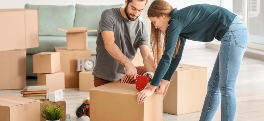 A couple in a room full of boxes taping them up preparing to move house