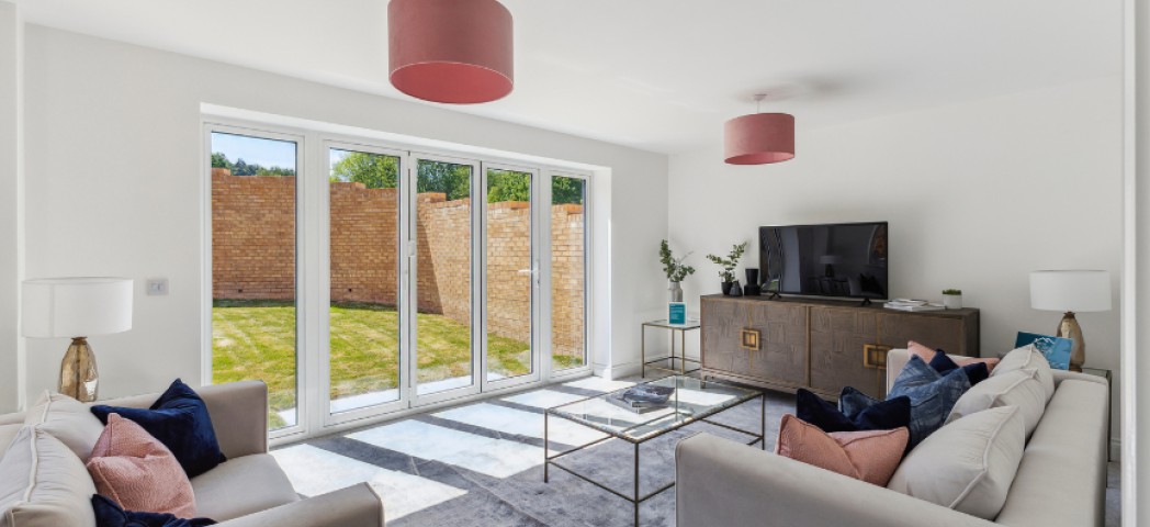 A new-build living room with white walls, patio doors leading to a sunny garden and stylish furniture inside