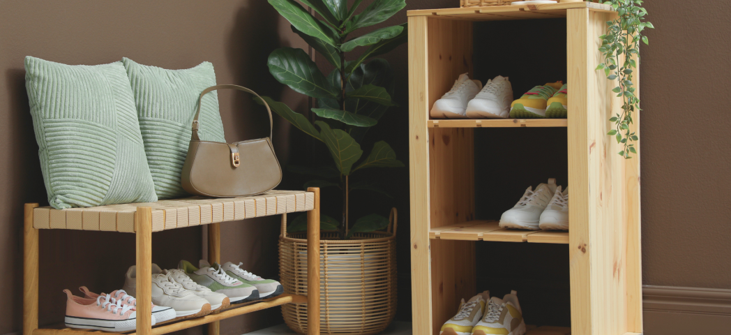 Wooden shoe bench and shelving unit with neatly arranged shoes, cushions, a handbag, and a houseplant.