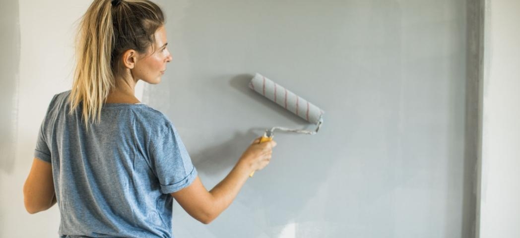 A woman with blonde hair is painting a wall with a paint roller.
