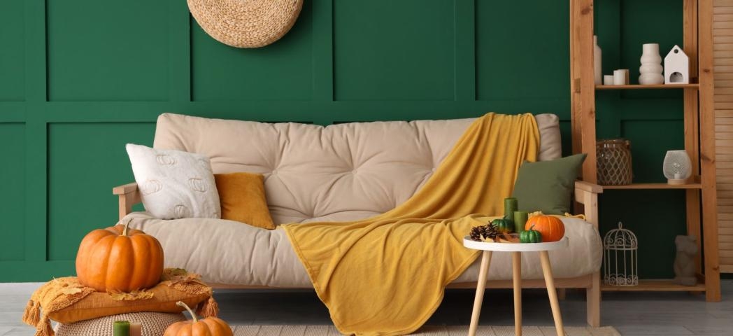 Cosy autumn living room with a cream sofa, mustard throw, pumpkins and a dark green feature wall.