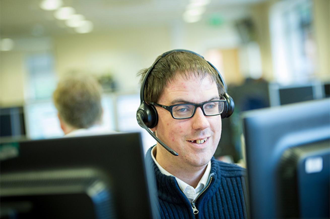 Disability confident employer Sanctuary employee Matthew wearing a headset sitting at a bank of computers