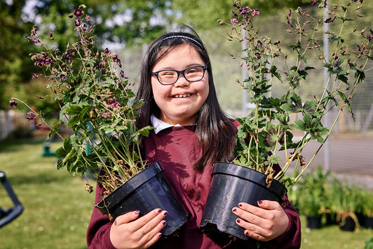 Plants ready to be added to the sensory garden. An image showing a student at the school holding two plants.