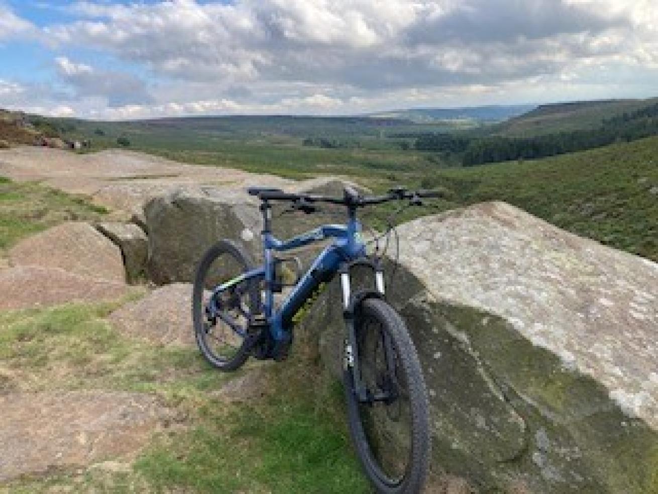 An e-bike propped up against a stone wall in the middle of fields with hills in the background