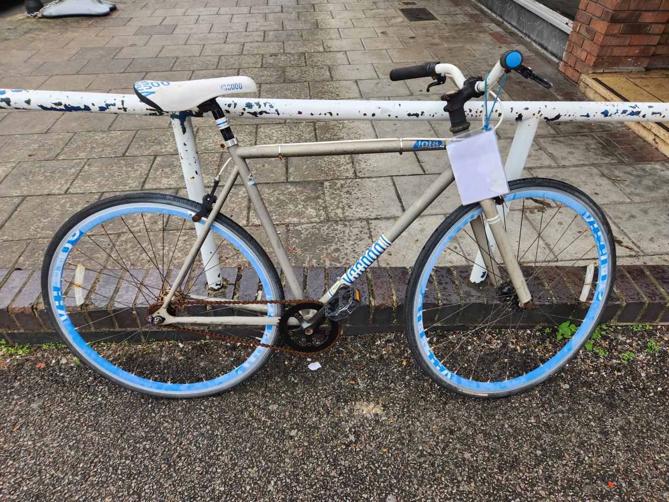 A white bike with blue and black wheels leaning on a white metal railing