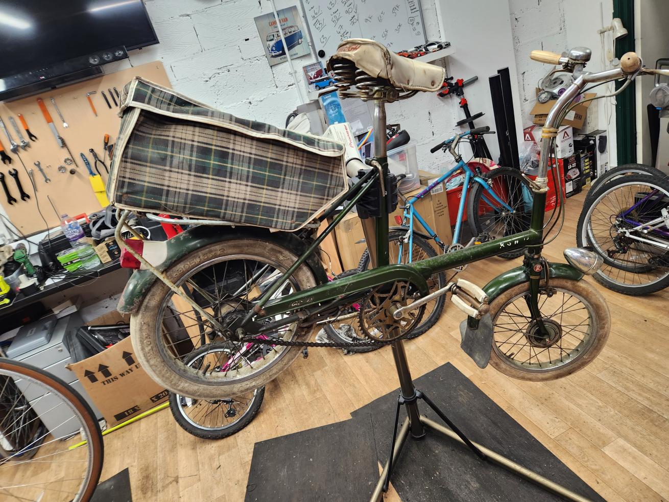 A bike with a tartan carry case suspended on a stand inside a workshop surrounded by tools