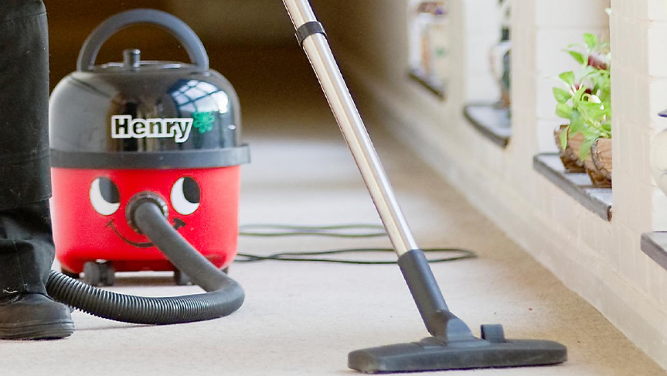 Somebody cleaning a carpet next to a wall using a Henry hoover