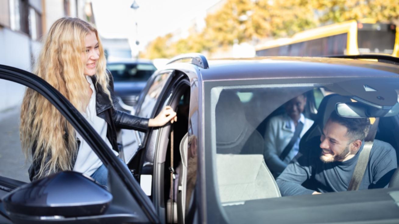 Stock image of a young woman getting into a car with her friends