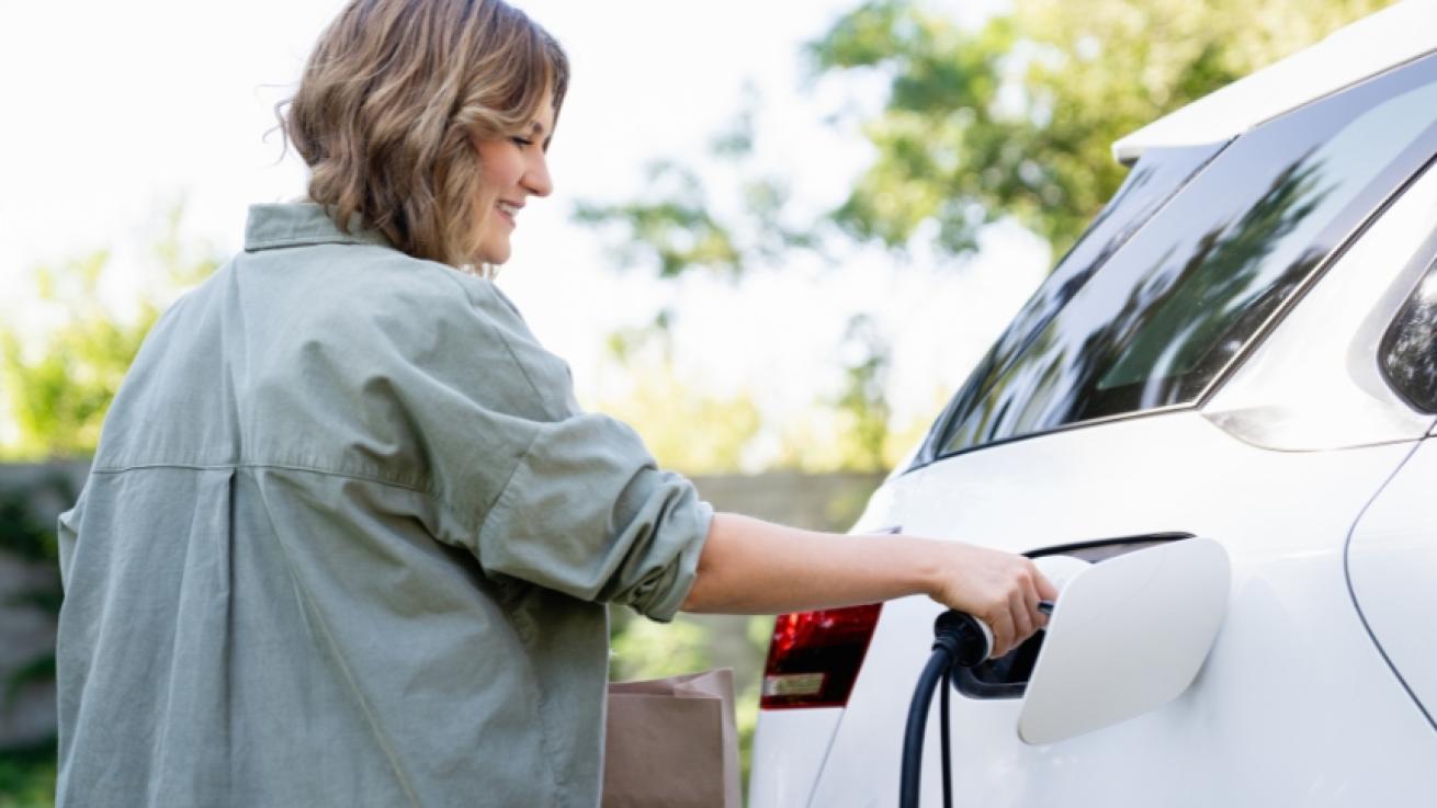 Stock image of a young woman plugging in the charger of her electric car