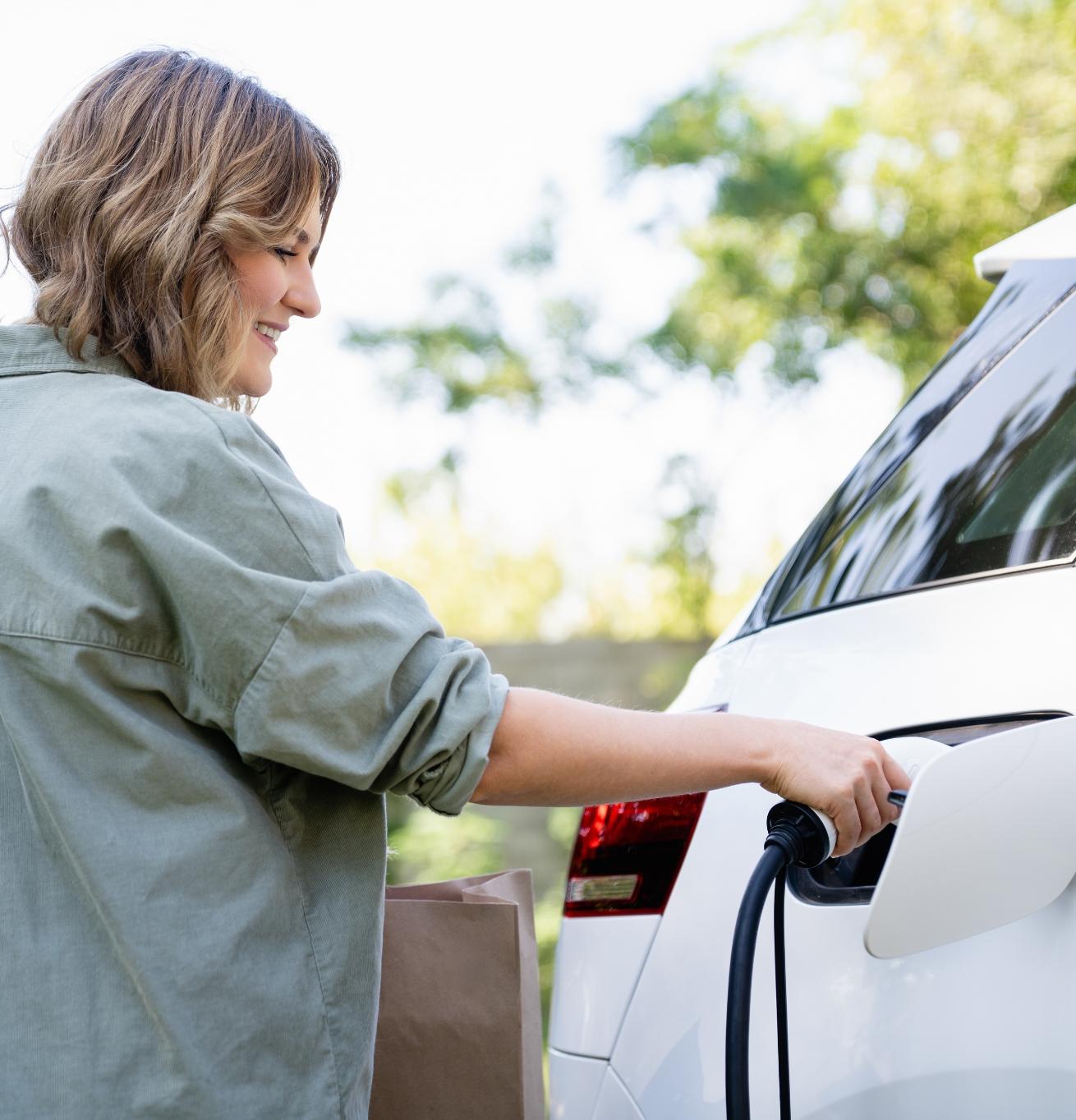 Stock image of a young woman plugging in the charger of her electric car