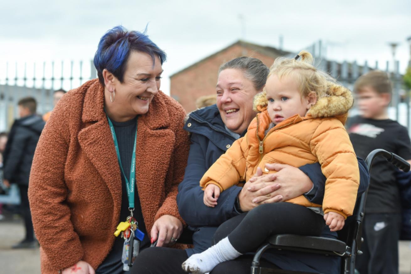Housing Office smiling at a Sanctuary resident who is also smiling and holding a small child