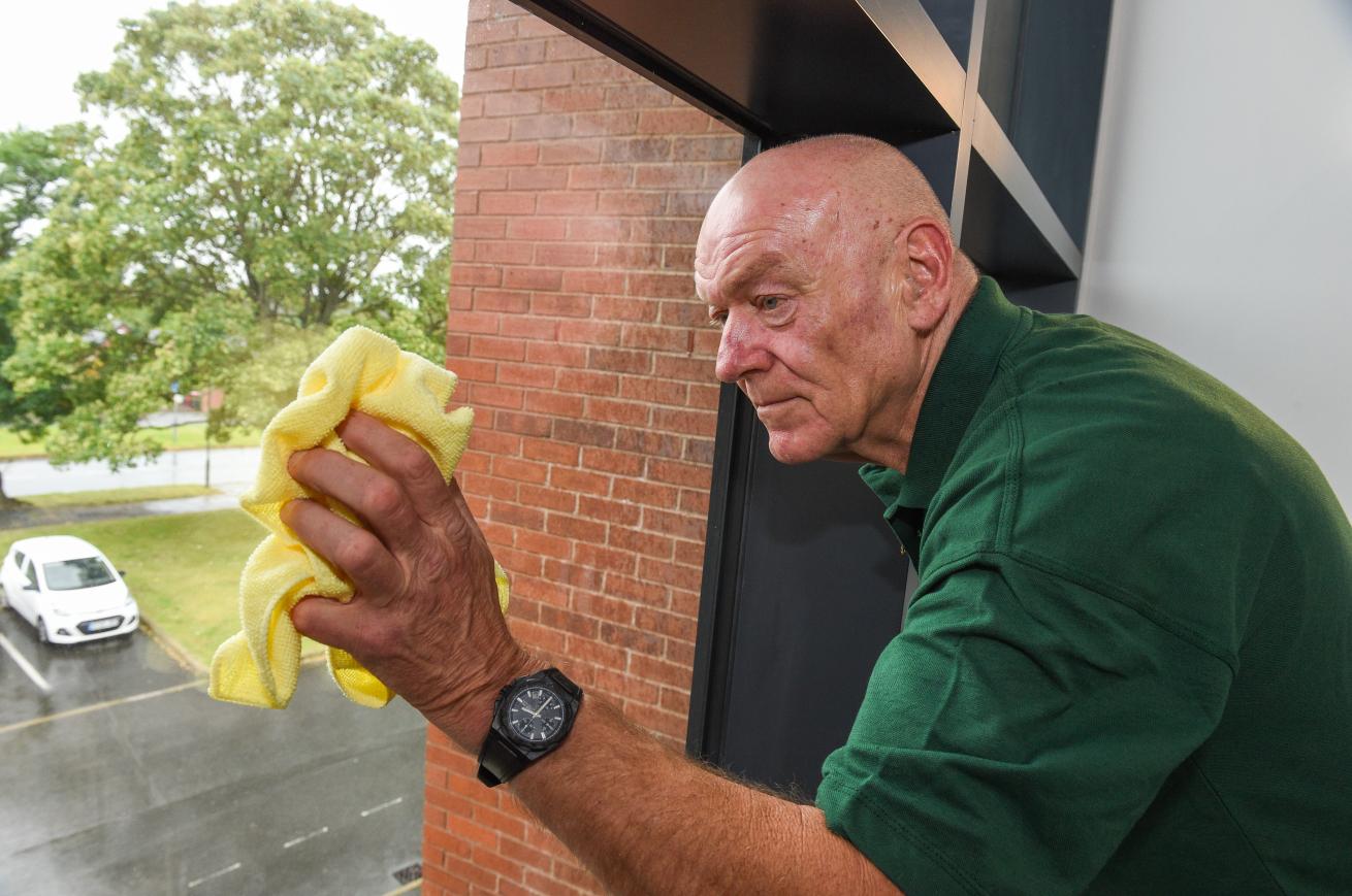 A person wearing a green shirt using a yellow cloth to clean a window