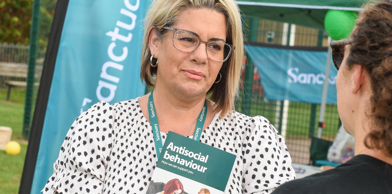 Two people engaging in conversation at an outdoor event, one is holding a pamphlet titled "Antisocial behaviour: How we can support you."